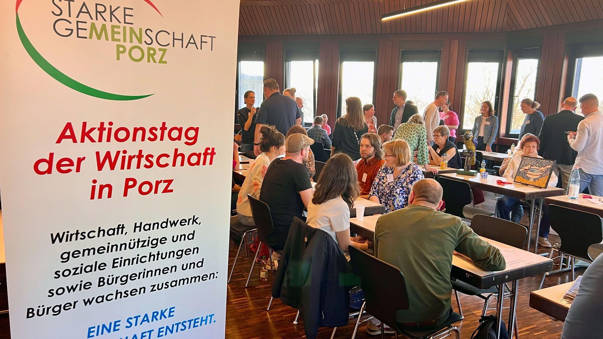 An Konferenztischen sitzen Menschen, andere gehen an den Tischen entlang.