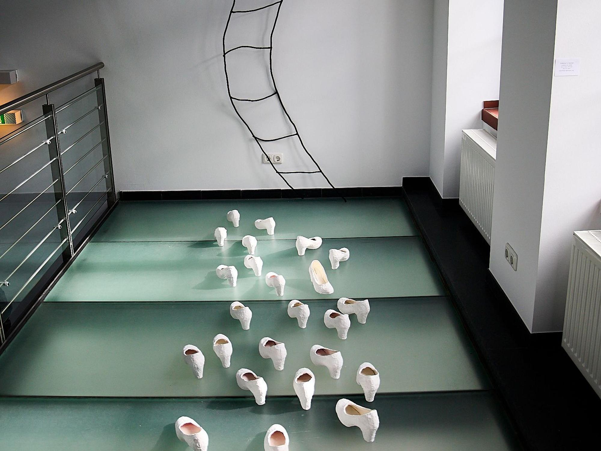 In der Kunst-Installation „Stairway to heaven“ von Dorothee Hermann sind weiße Pumps zu sehen. Sie sind auf eine Wand ausgerichtet, an der eine geschwungene Leiter nach oben führt.