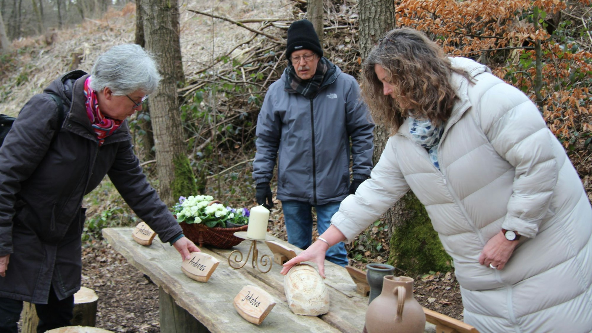 Drei Frauen stellen auf einem Holztisch im Wald das Letzte Abendmahl nach.