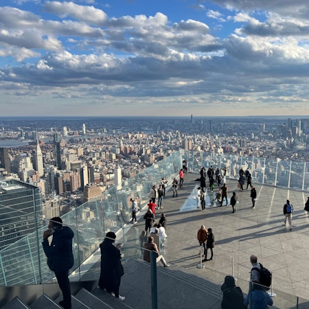 Menschen auf einer Aussichtsplattform, im Hintergrund Wolkenkratzer von Manhattan.