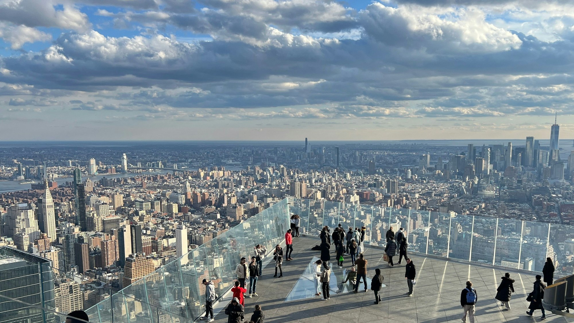 Menschen auf einer Aussichtsplattform, im Hintergrund Wolkenkratzer von Manhattan.