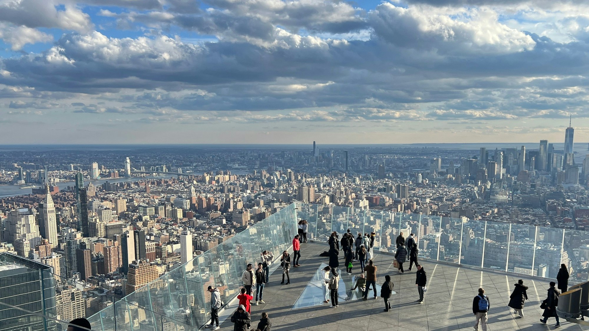 Menschen auf einer Aussichtsplattform, im Hintergrund Wolkenkratzer von Manhattan.