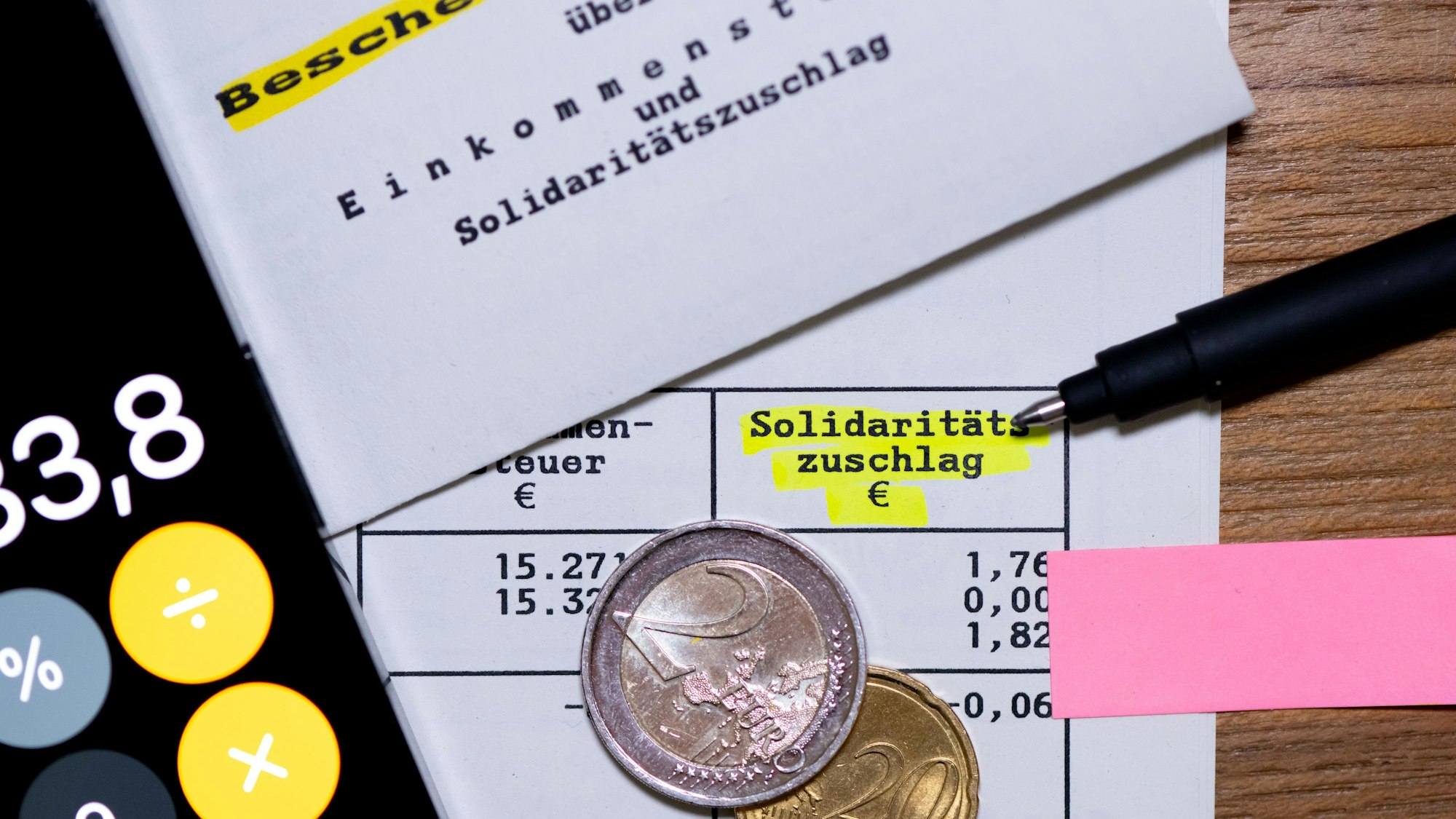 Das Wort „Solidaritätszuschlag“ ist neben einem Taschenrechner und einem Stift auf einem Steuerbescheid zu sehen. (Symbolbild)