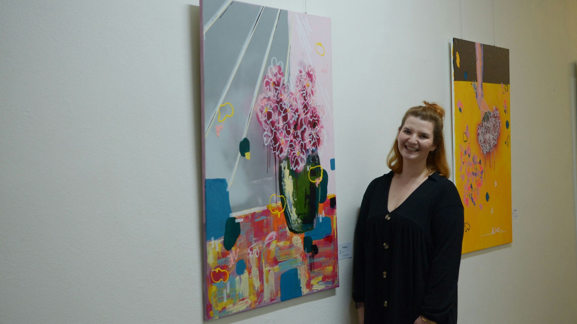 Das Bild zeigt Denise Wagner vor zwei Gemälden, die in einem Flur des Rathauses hängen.