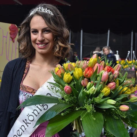 Das Foto zeigt eine Frau mit Schärpe, Krone und einem großen Strauß Tulpen.
