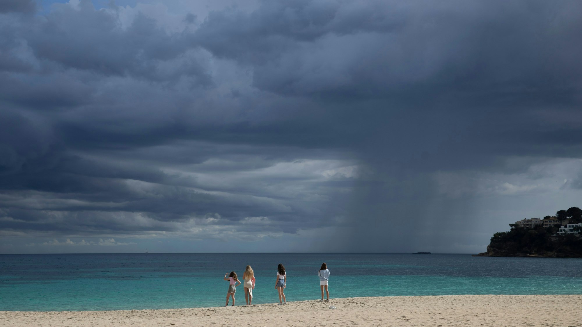 Eine Gruppe von Touristen steht am Meer an einem bewölkten Tag am Strand von Magaluf auf Mallorca.