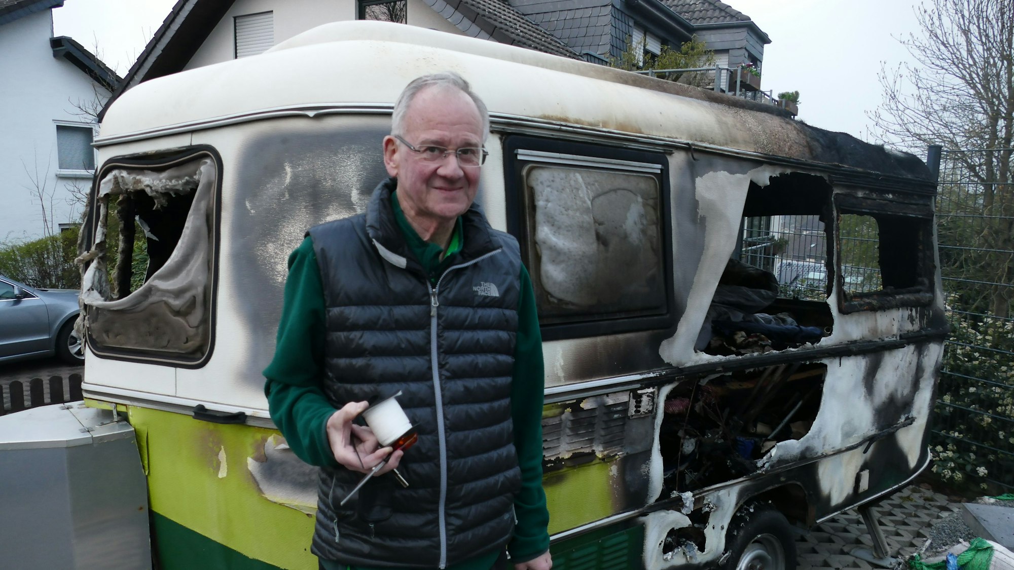 Ein Mann steht vor einem von Feuer völlig zestörten Wohnwagen.
