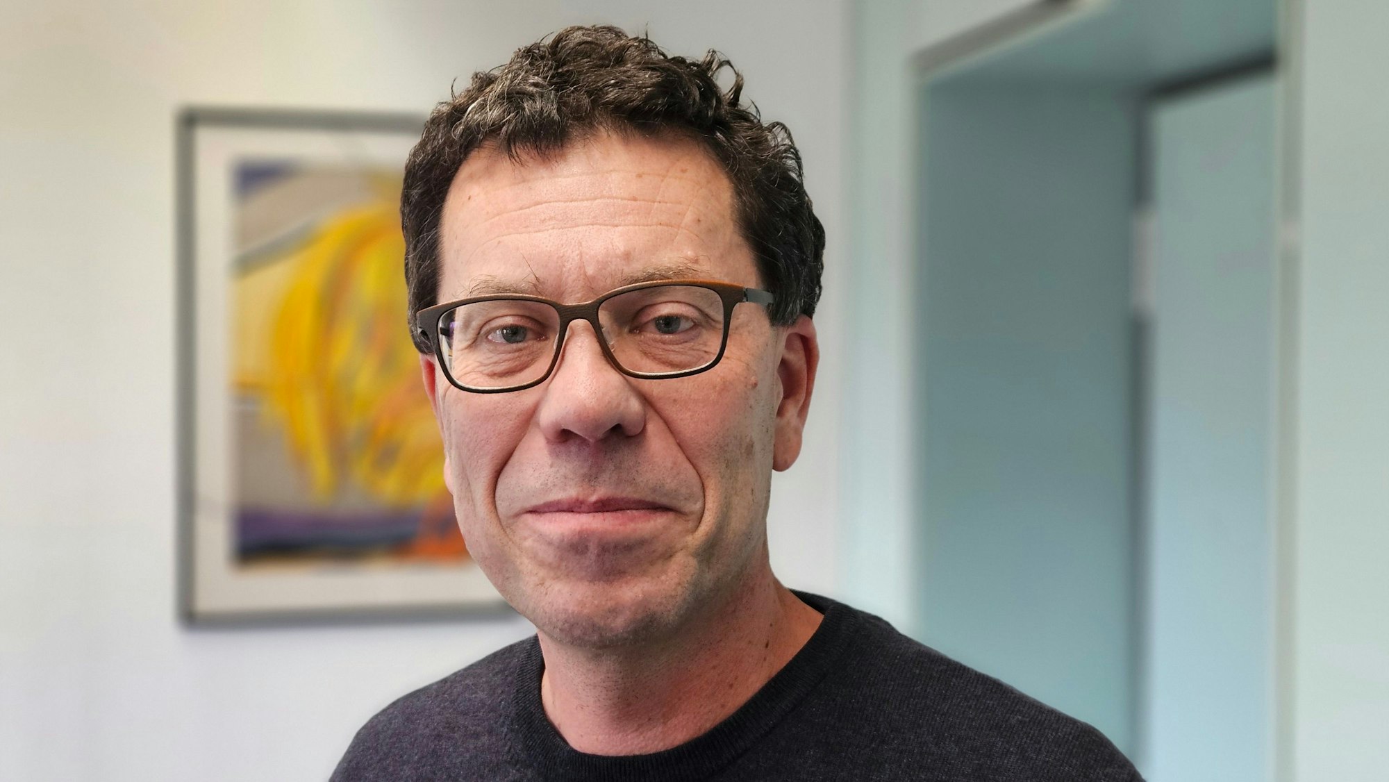 Auf dem Foto ist ein Mann mit Brille zu sehen. Er trägt einen dunklen Pullover.