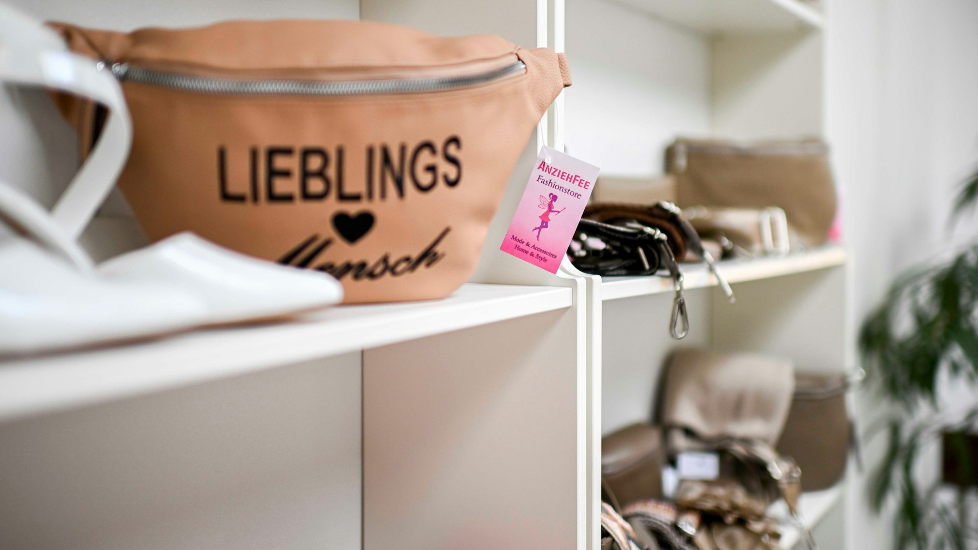 In einem weißen Regal des Modegeschäftes werden unterschiedliche Taschen zum Kauf angeboten.