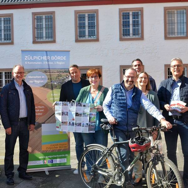 Mehrere Frauen und Männer stehen mit einer Faltkarte und einem Fahrrad vor einem Roll-up-Display mit der Aufschrift „Zülpicher Börde“.