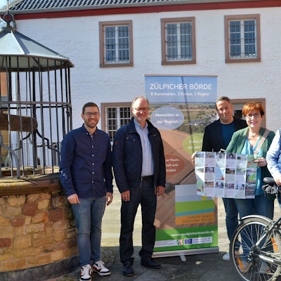Mehrere Frauen und Männer stehen mit einer Faltkarte und einem Fahrrad vor einem Roll-up-Display mit der Aufschrift „Zülpicher Börde“.
