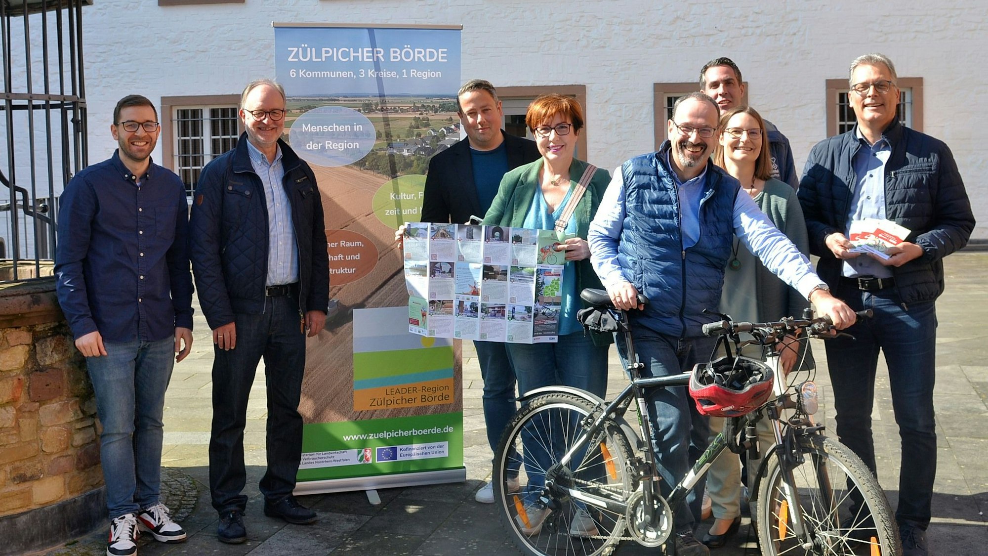 Mehrere Frauen und Männer stehen mit einer Faltkarte und einem Fahrrad vor einem Roll-up-Display mit der Aufschrift „Zülpicher Börde“.