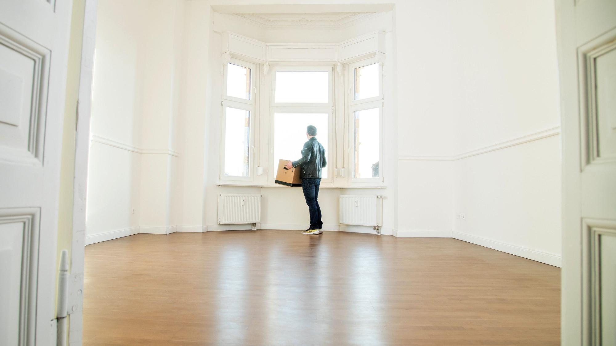 Eine Person steht mit einer Umzugskiste in einer leeren Wohnung.