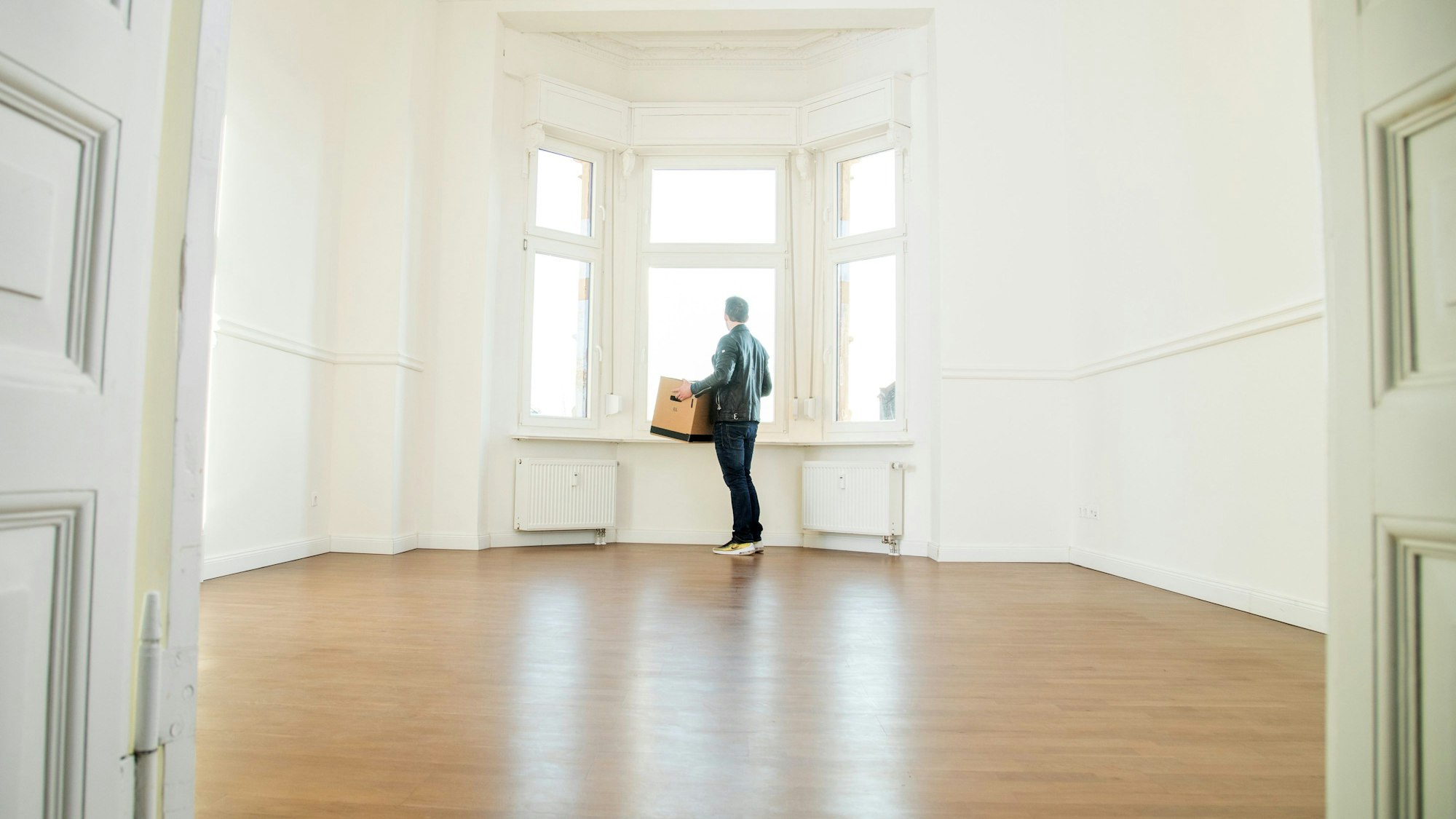 Eine Person steht mit einer Umzugskiste in einer leeren Wohnung.
