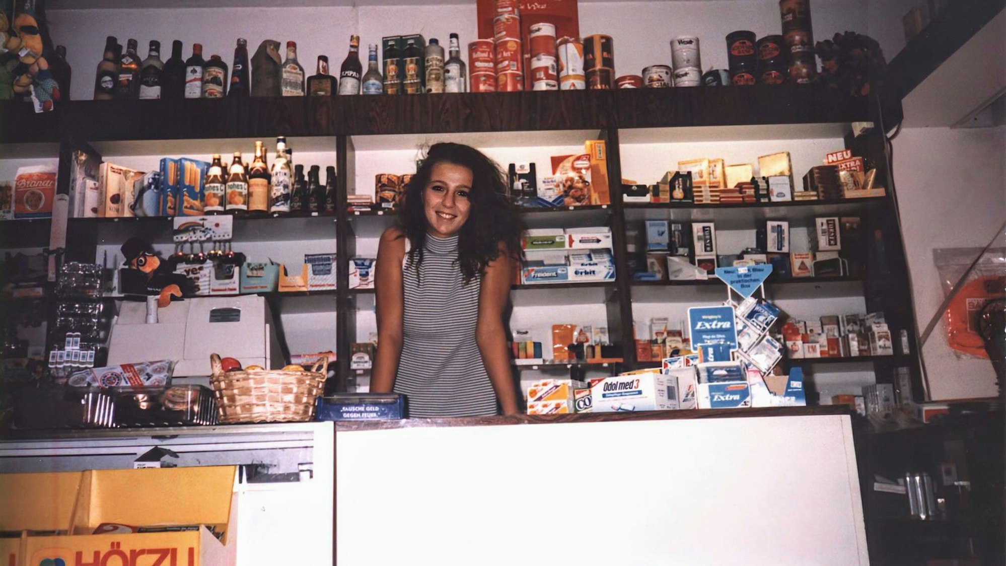 Eine junge Frau in einem Kiosk, im Hintergrund gefüllte Regale.