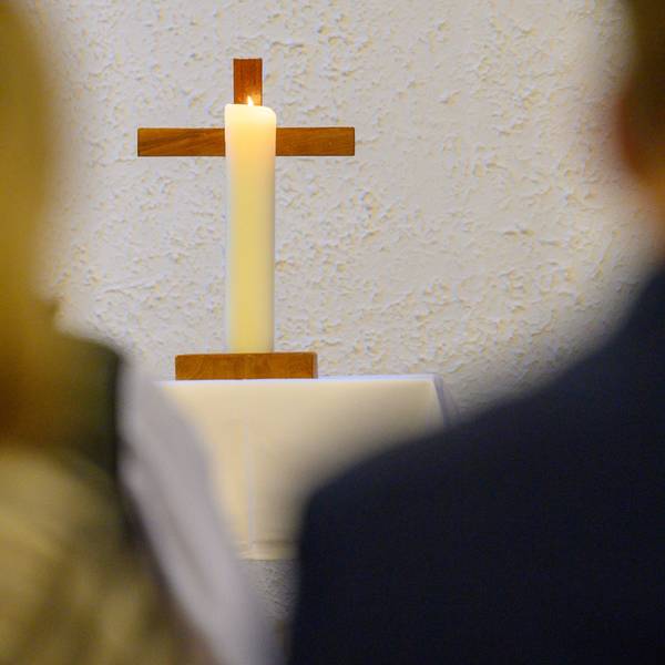 Eine Kerze brennt vor einem Kreuz.