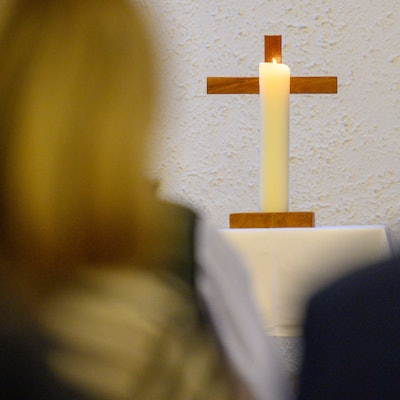 Eine Kerze brennt vor einem Kreuz.