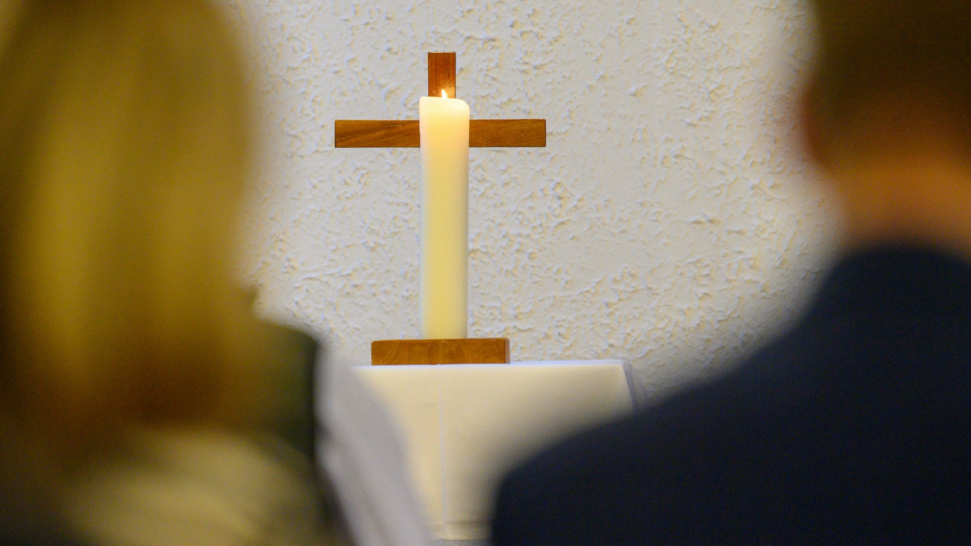 Eine Kerze brennt vor einem Kreuz.