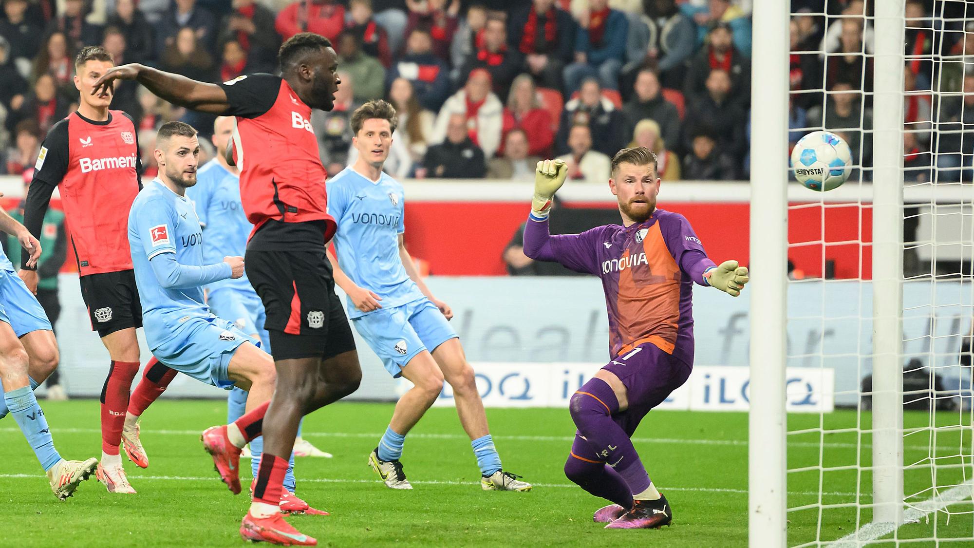 Victor Boniface (M) von Bayer 04 Leverkusen erzielt das Tor zum 2:1 gegen Torwart Timo Horn vom VfL Bochum.