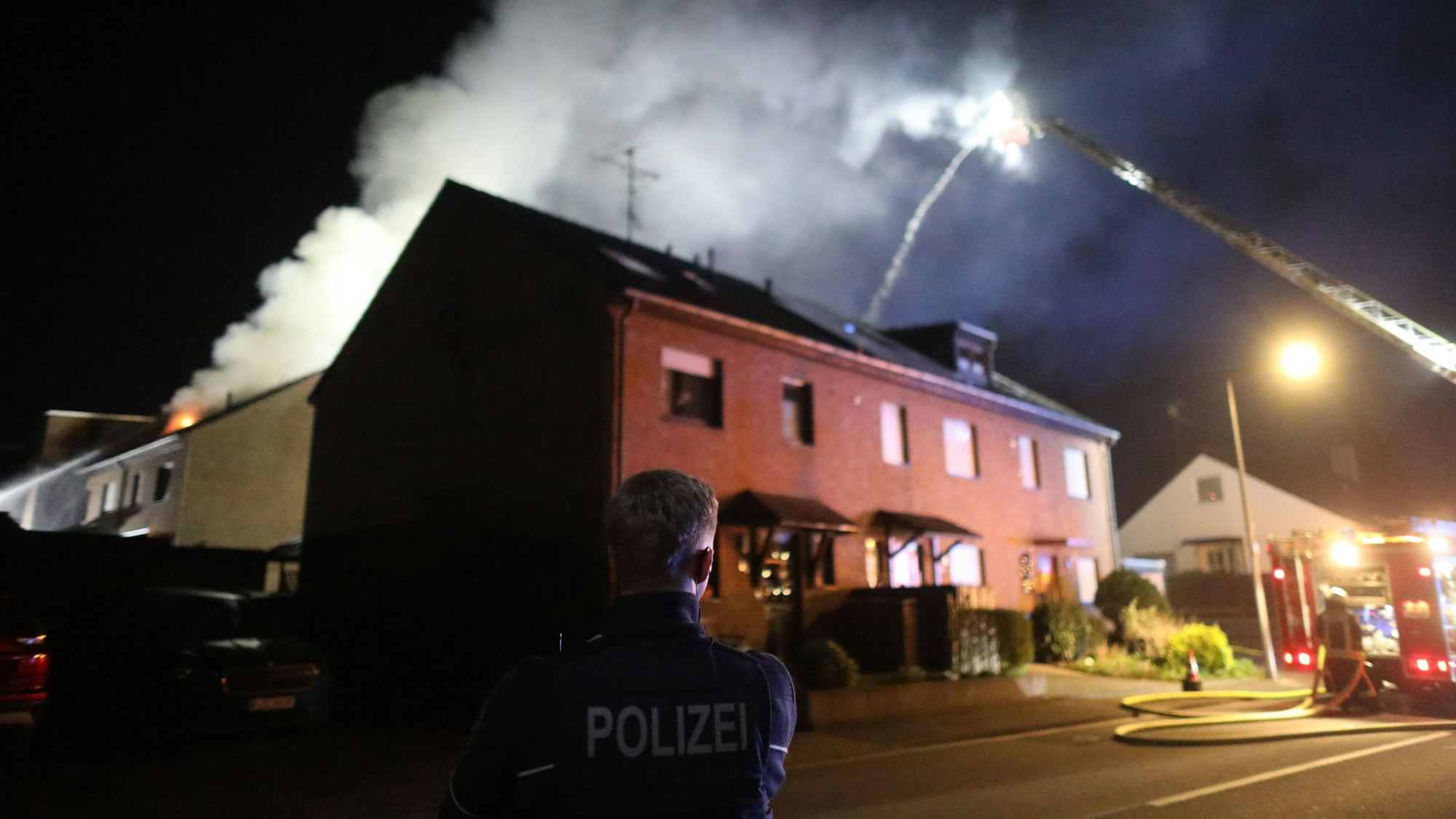 Ein Polizist steht in Lind auf der Straße und sichert den Einsatz der Feuerwehr. Am Donnerstagabend kam es in dem Kölner Stadtteil zu einem Dachstuhlbrand.
