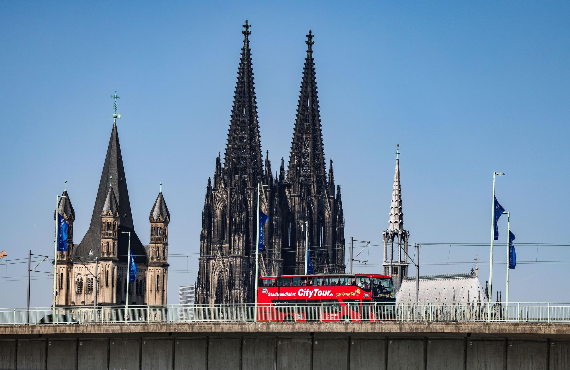 Köln: Ein City-Tour Bus fährt bei sonnigem Wetter am Dom vorbei über die Deutzer Brücke.