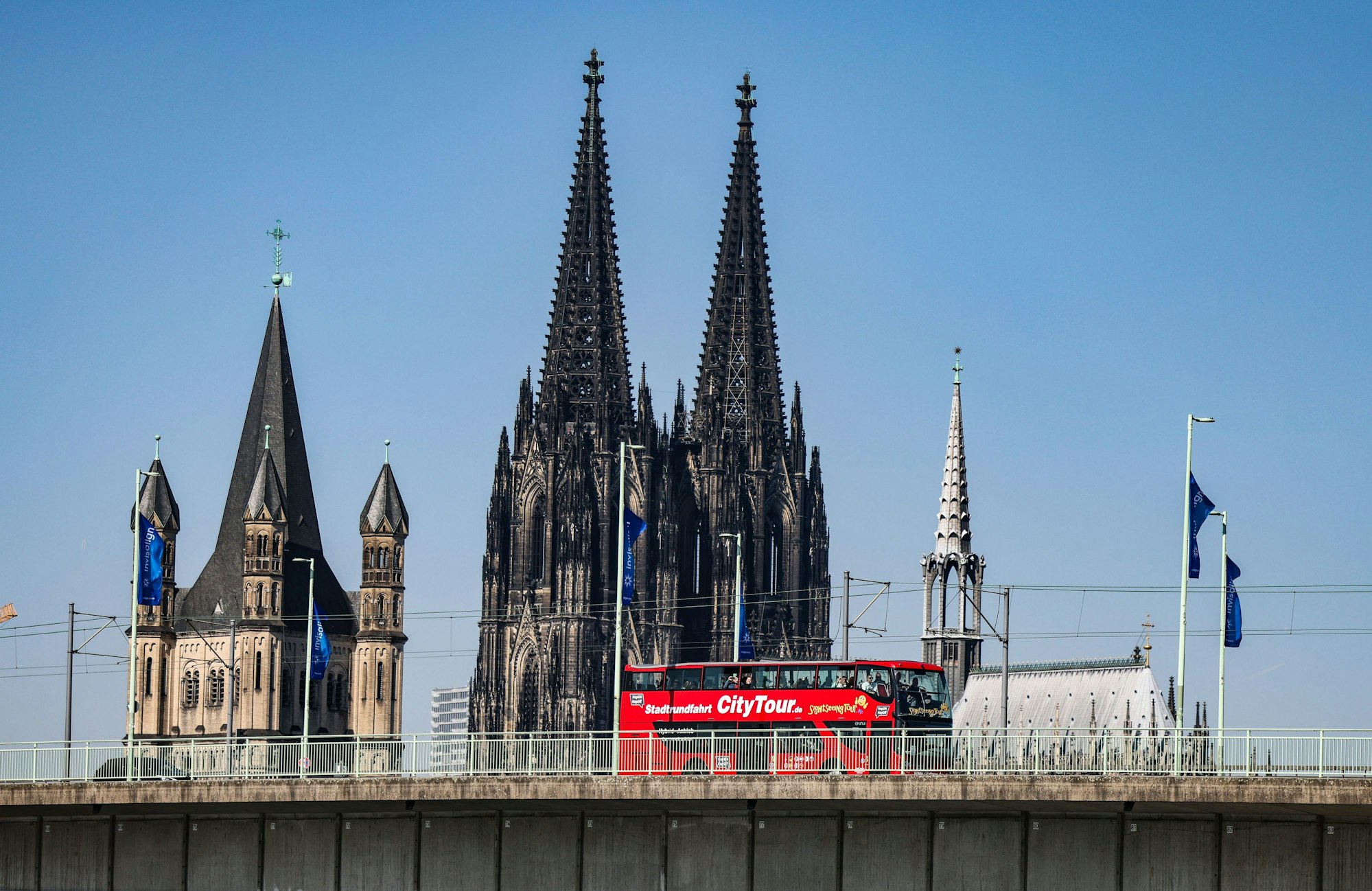 Köln: Ein City-Tour Bus fährt bei sonnigem Wetter am Dom vorbei über die Deutzer Brücke.