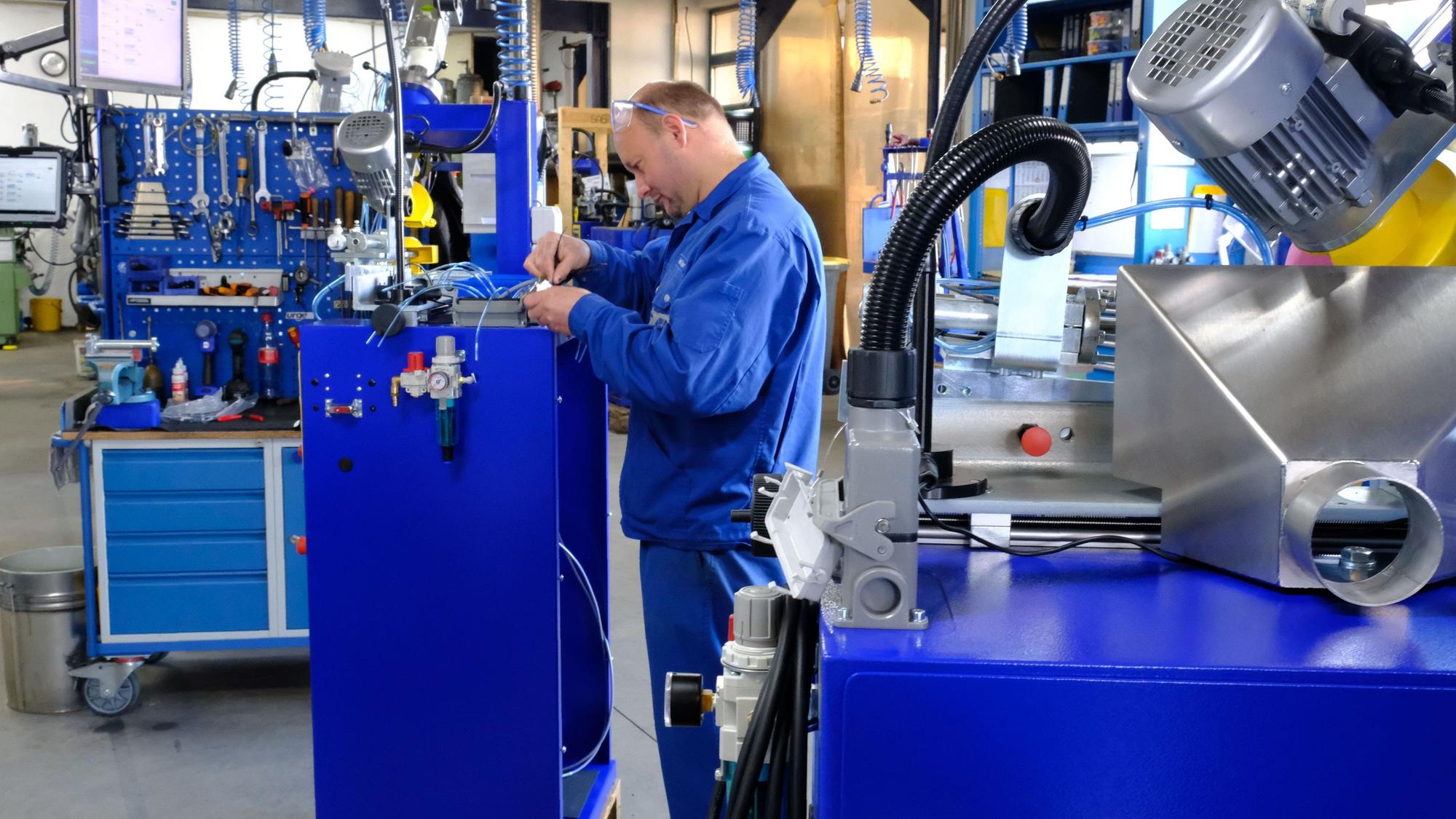 Ein Mitarbeiter der Firma Franzen in blauer Arbeitskleidung bei der Montage eines Kettenschärfautomaten.
