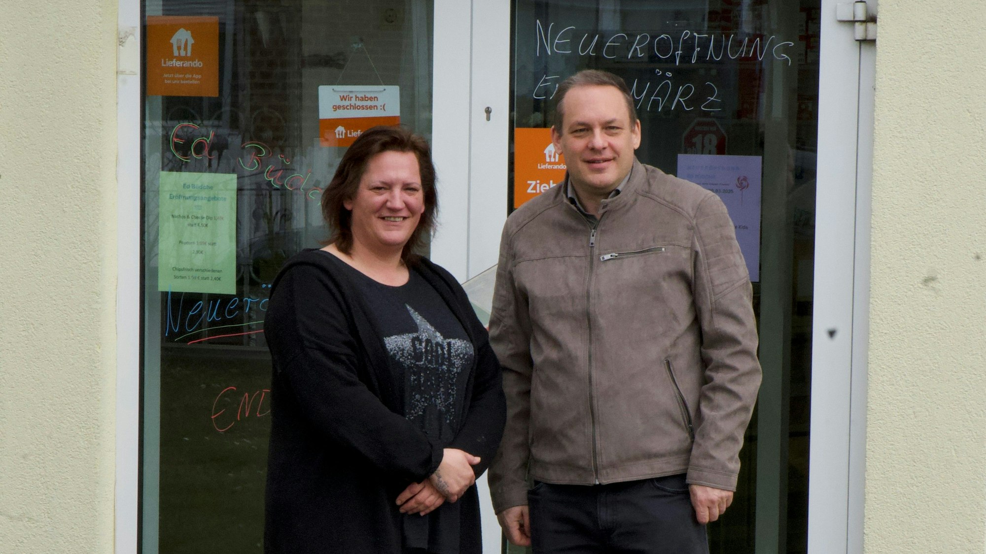 Zwei Menschen lächeln und stehen vor einer Tür.