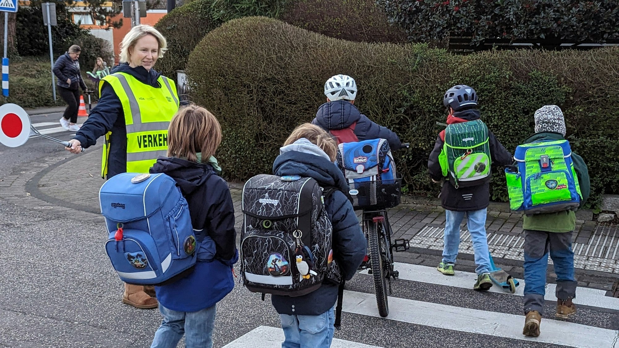 Das Foto zeigt eine Mutter, die Kindern über einen Zebrastreifen hilft.