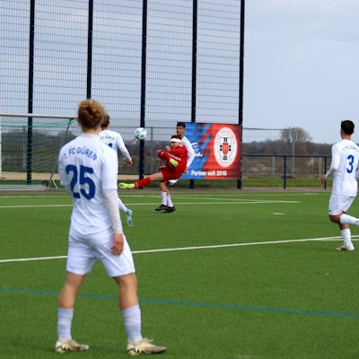 Ein Fußballspieler mit einem Kopfverband versucht einen Seitfallzieher.