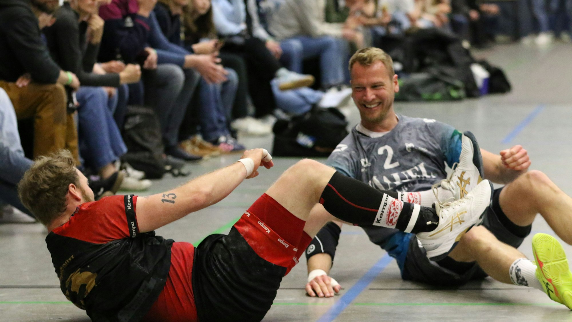 Zwei Handballer liege am Boden und lachen sich an.