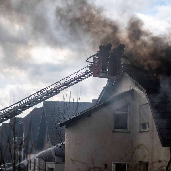 Das Bild zeigt zwei Feuerwehrleute im Korb einer Drehleiter. Sie bekämpfen im dichten Rauch einen Dachstuhlbrand.