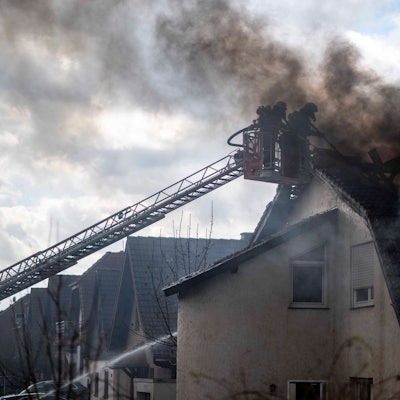 Das Bild zeigt zwei Feuerwehrleute im Korb einer Drehleiter. Sie bekämpfen im dichten Rauch einen Dachstuhlbrand.