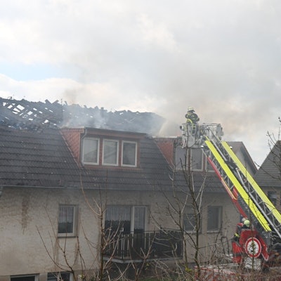 Feuerwehrleute löschen von einer Drehleiter aus den Brand im Dachstuhl eines Mehrfamilienhauses in Zülpich-Dürscheven.