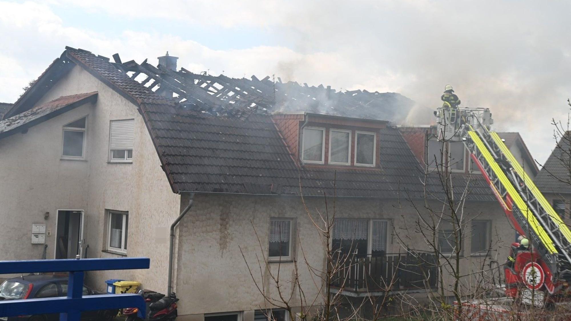 Feuerwehrleute löschen von einer Drehleiter aus den Brand im Dachstuhl eines Mehrfamilienhauses in Zülpich-Dürscheven.