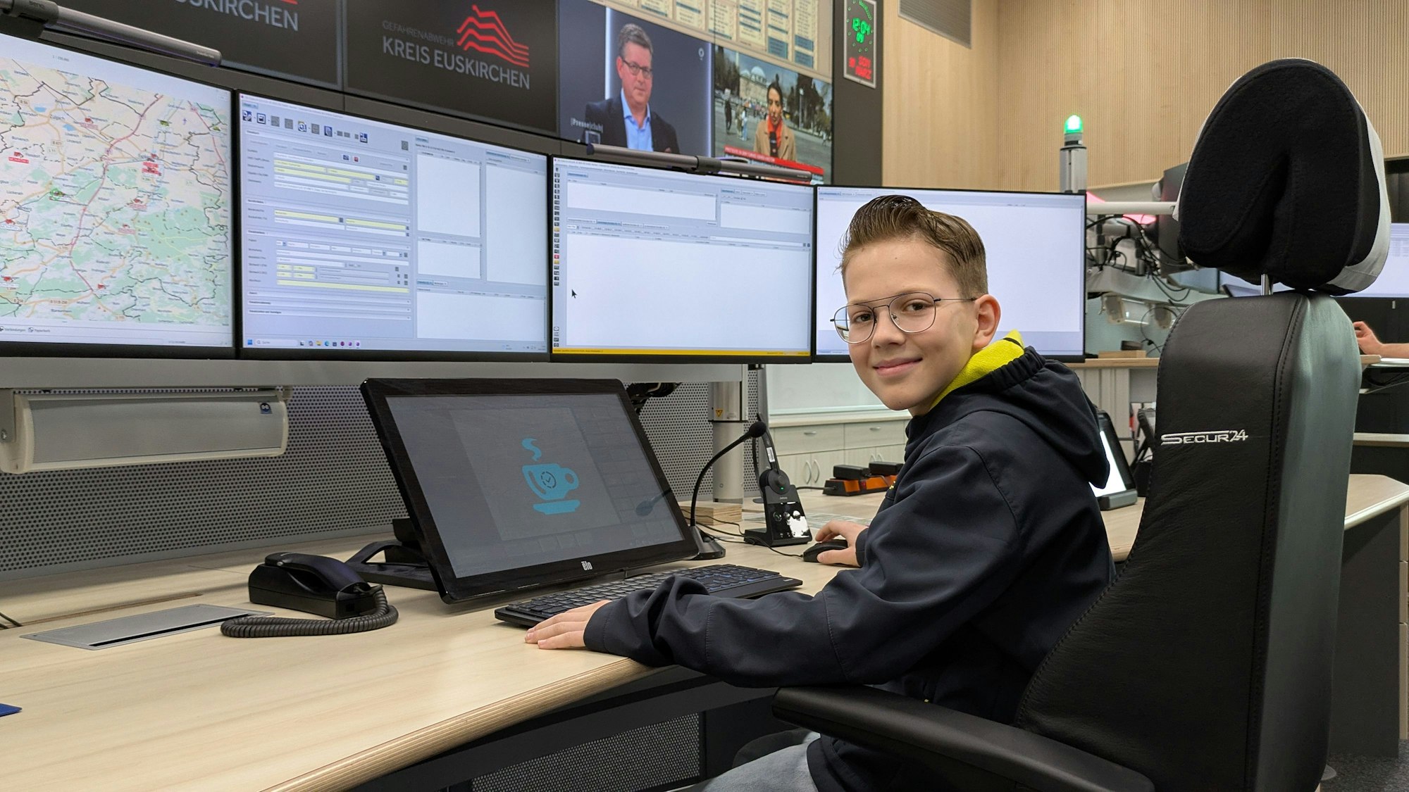 Ein junger Besucher hat vor mehreren Bildschirmen und einer großen Bildschirmwand Platz genommen.