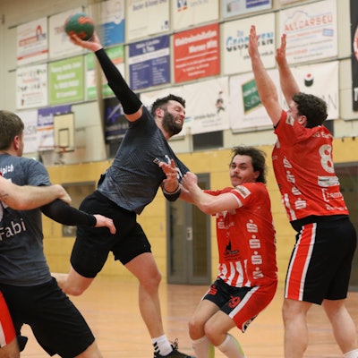 Daniel Schüller nimmt all seine Kraft zum Wurf zusammen. Sein Spielertrainer blockt den Weg frei. Ein Gegner zerrt an Schüllers Trikot, ein anderer reißt die Arme ur Abwehr hoch.