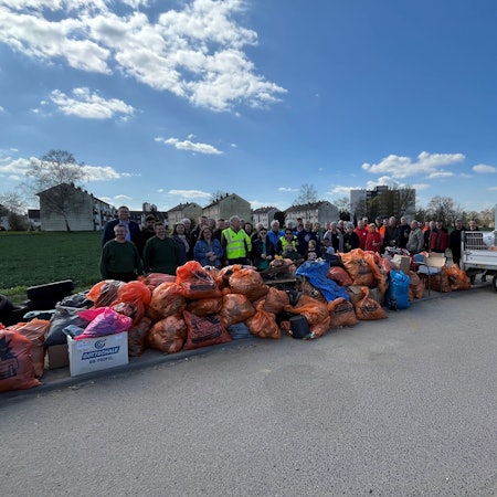 Freiwillige stehen vor zahlreichen orangen Müllsäcken.