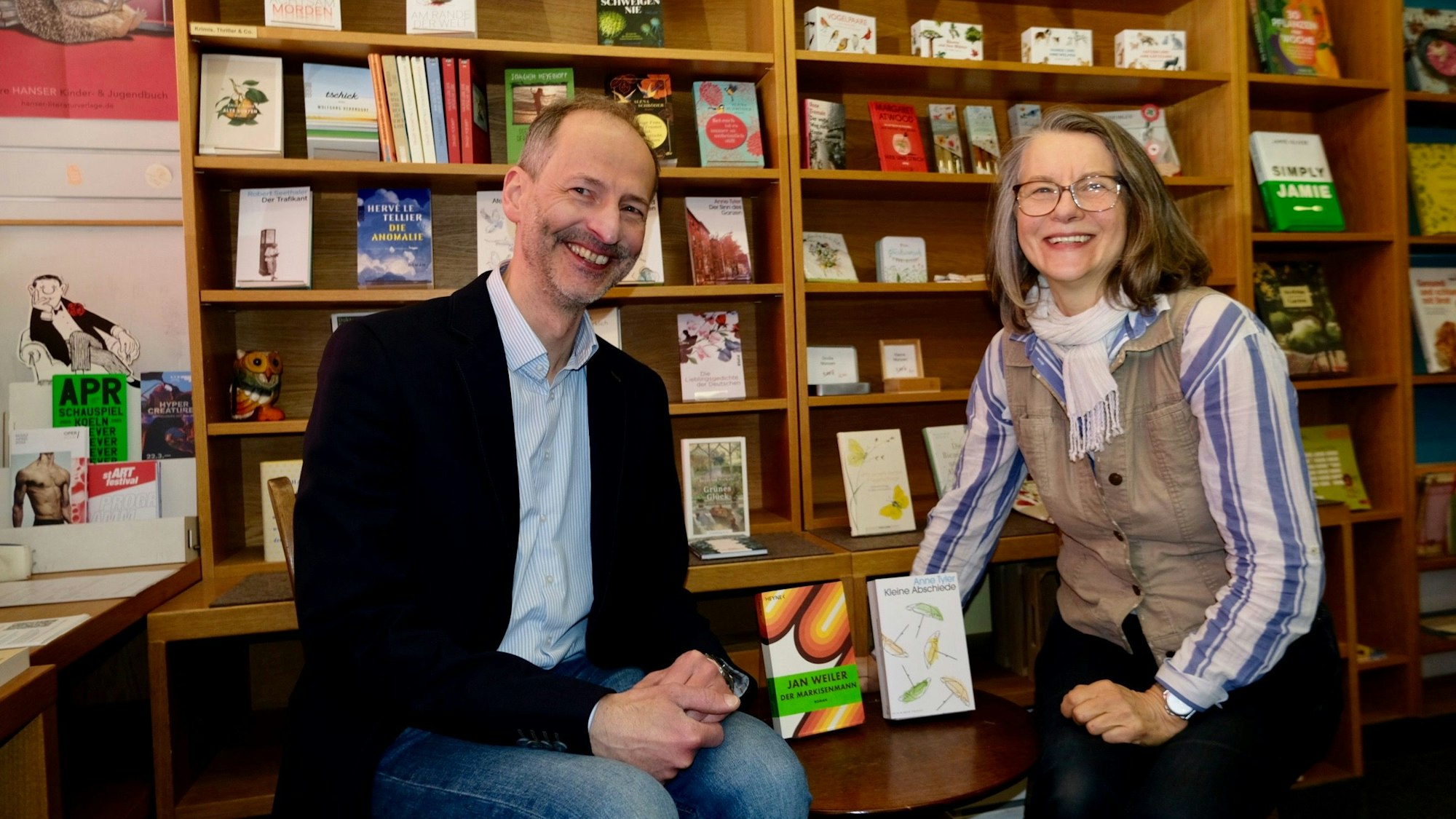 Ein Mann und eine Frau sitzen vor einem Bücherregal.