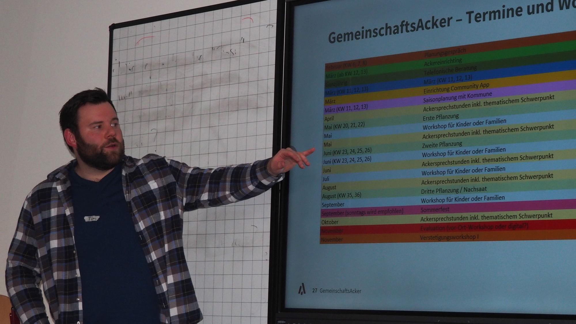 Tim Genders steht an einem Smartboard und stellt die Pläne für den Gemeindegarten vor.