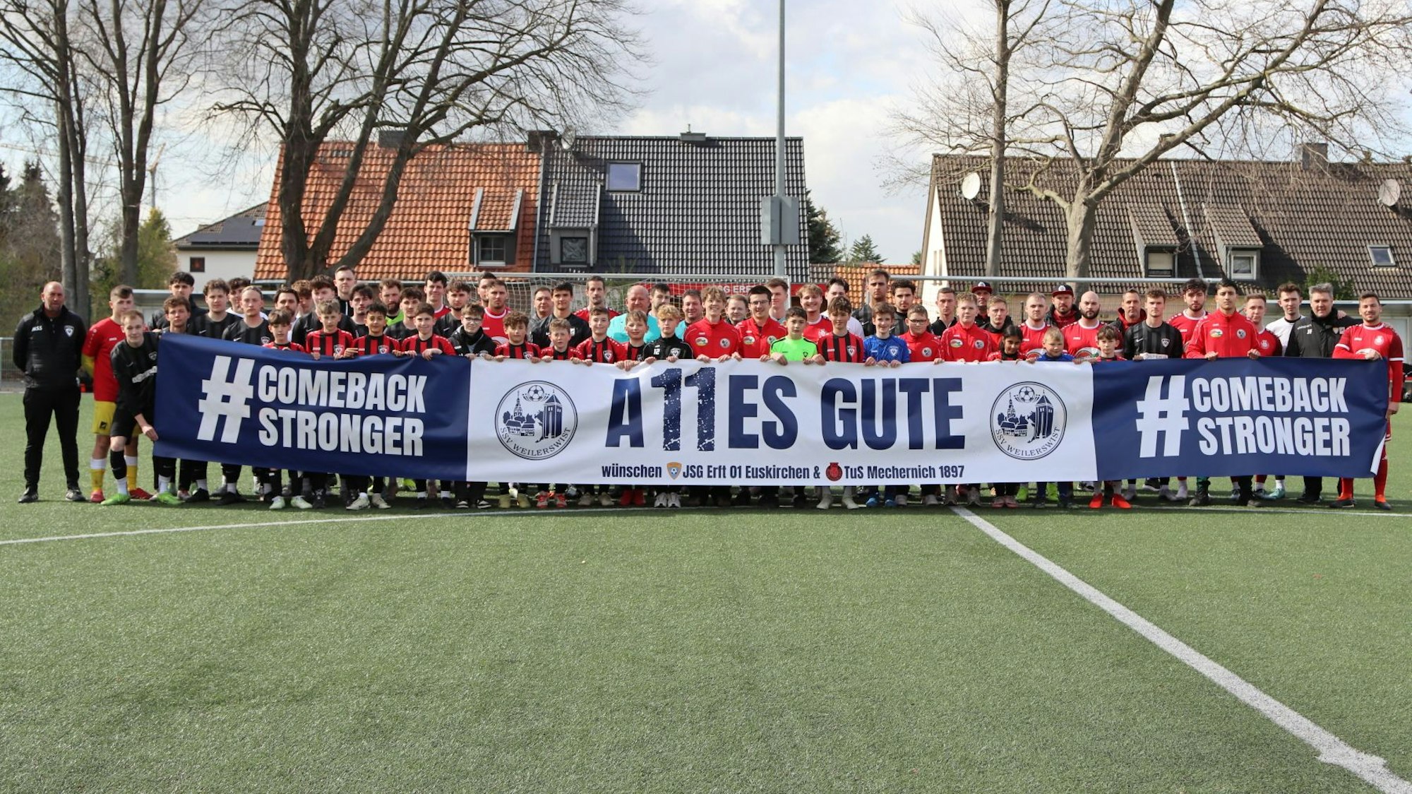 Das Bild zeigt die Mannschaften der JSG Erft Euskirchen und der TuS Mechernich, die vor dem Spiel ein Plakat hochhalten.
