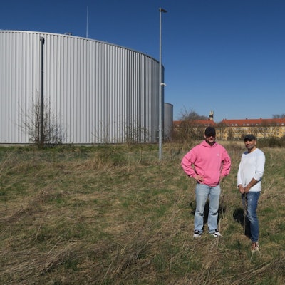 Zwei Männer stehen auf einer Wiese neben Wasserspeichern.