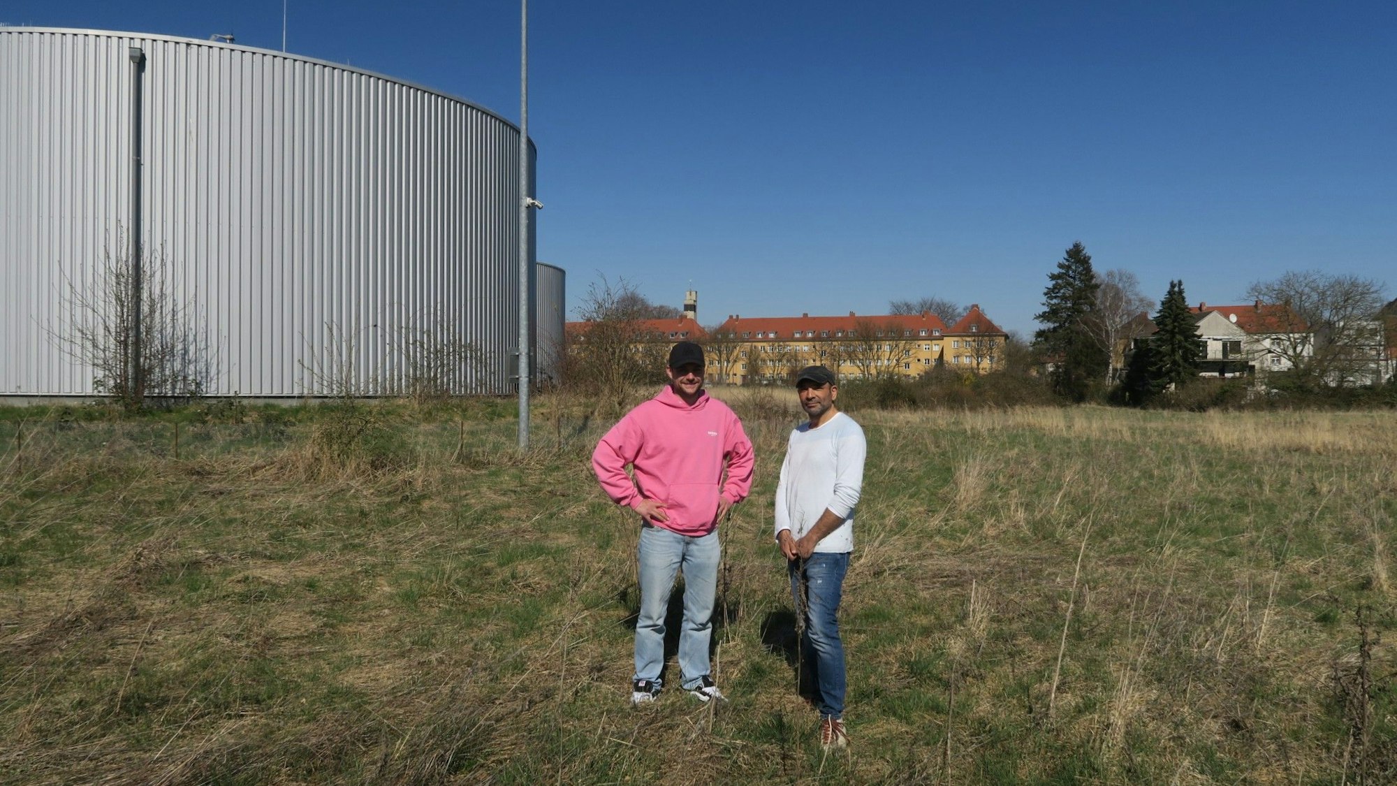 Zwei Männer stehen auf einer Wiese neben Wasserspeichern.