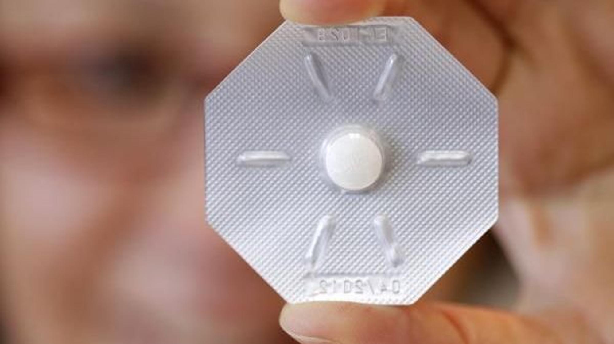Eine Frau hält ein Tabletten-Blister mit der „Pille danach“ vor ihr Auge.