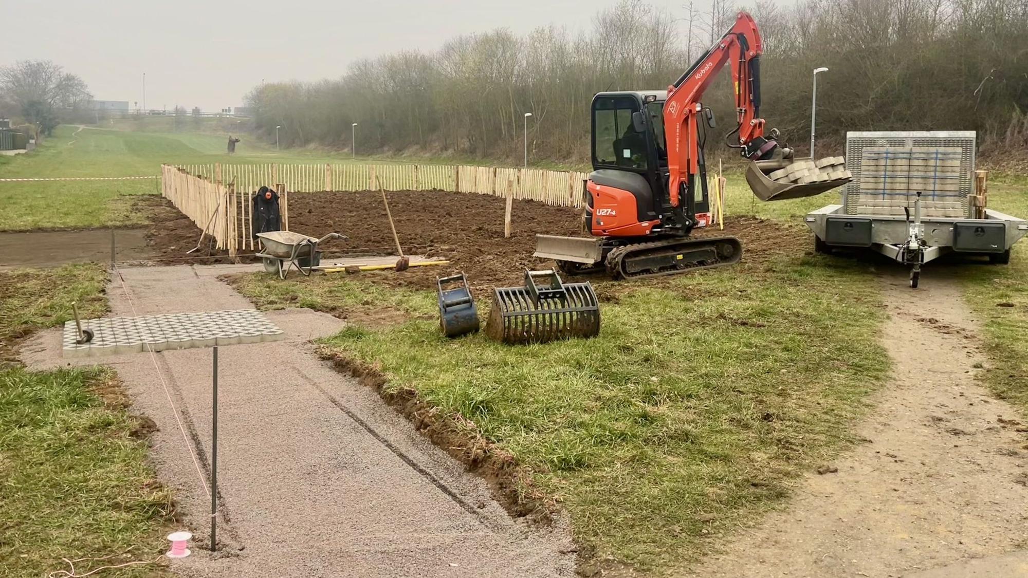 Ein Bagger steht auf der Fläche, die Gemeindeacker werden soll. Der Garten ist zum Teil schon eingezäunt.