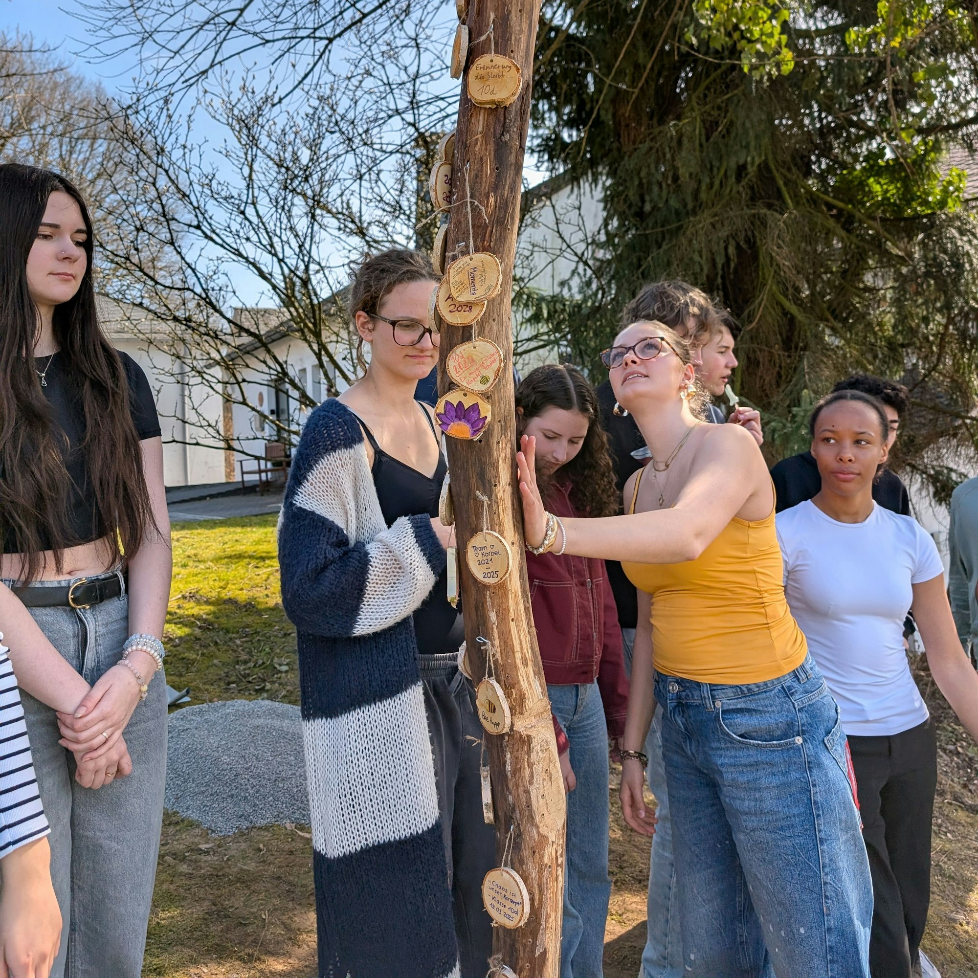Mehrere Schüler befestigen kleine gestaltete Holzscheiben an einem Totholz-Stamm.