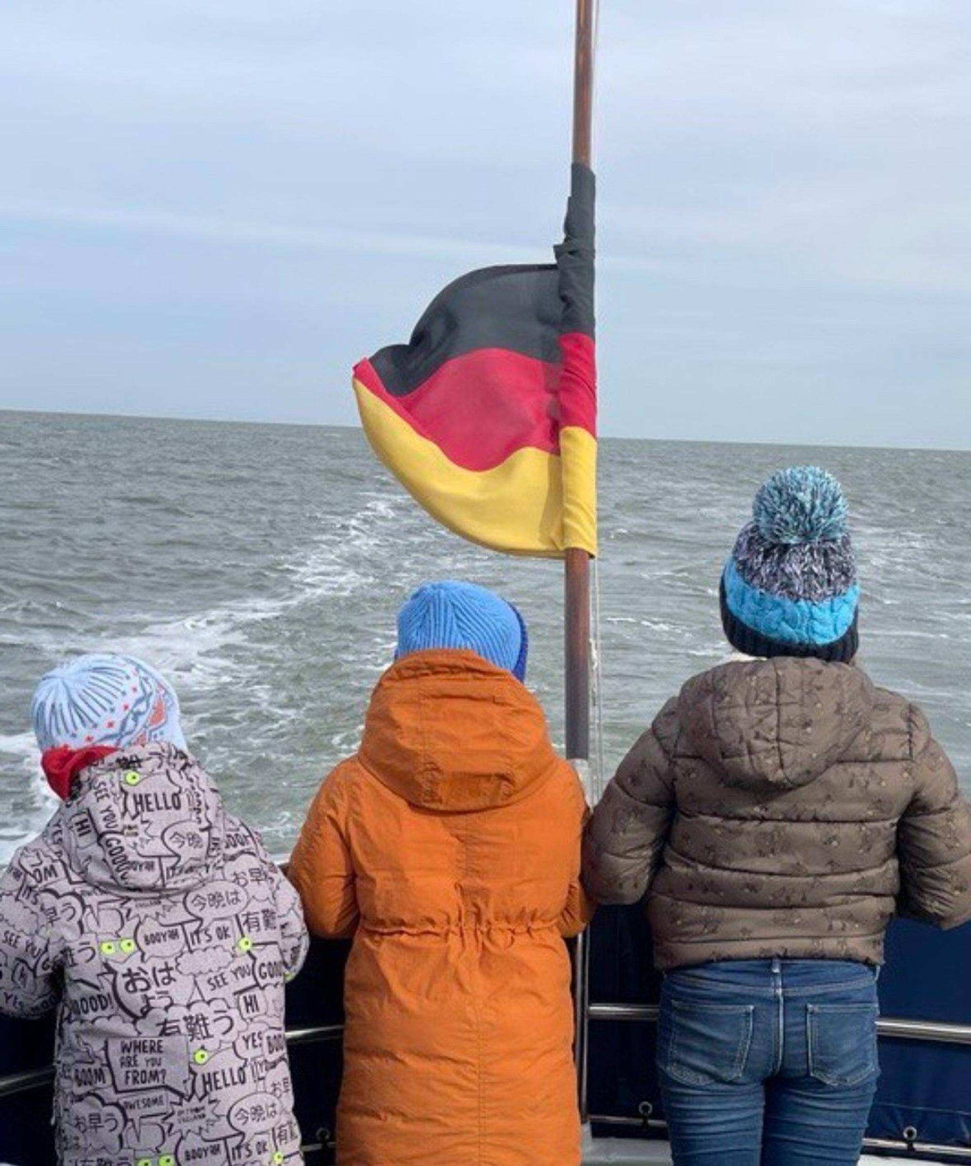 Das Foto zeigt drei kleine Kinder auf einem Schiff. Sie schauen auf die See.