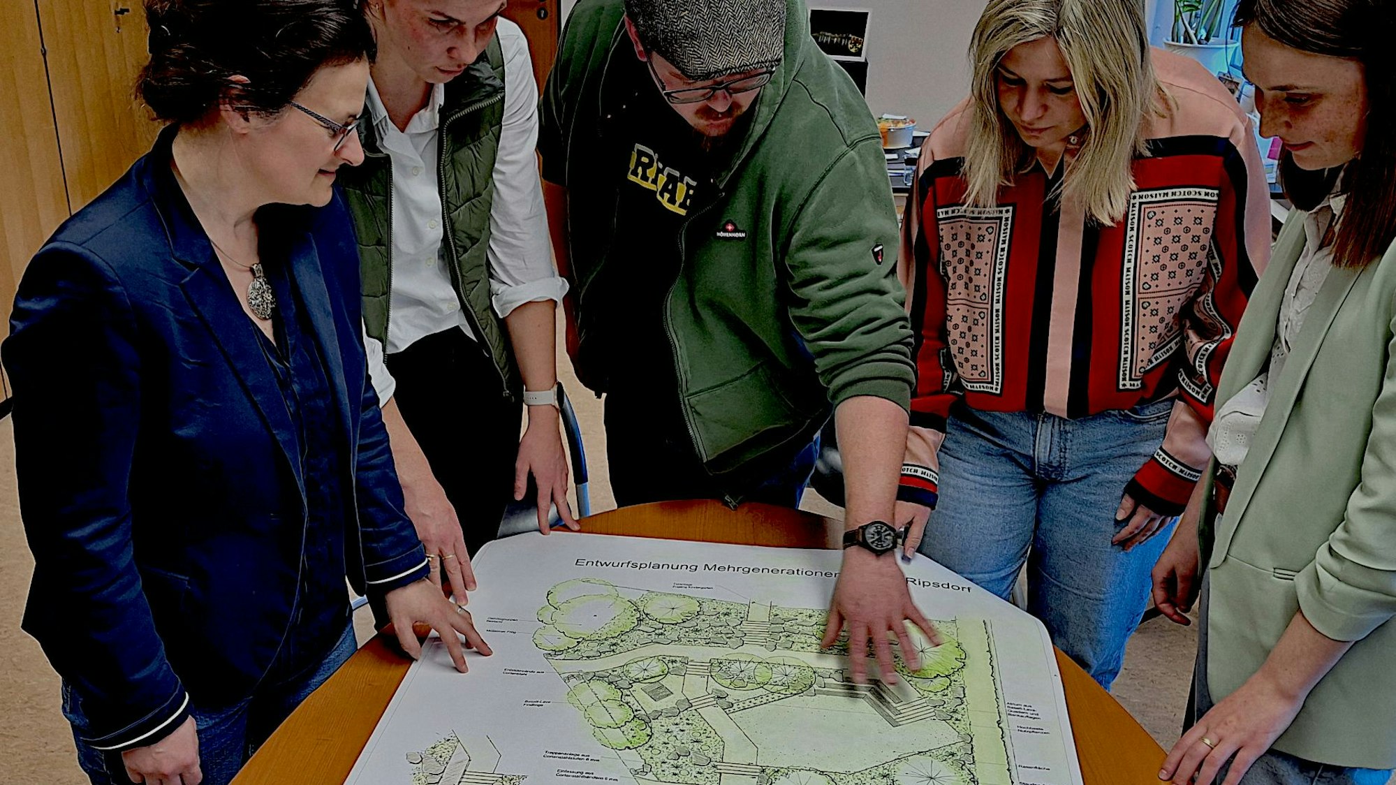Fünf Personen schauen auf einen Plan, der auf einem Tisch liegt.