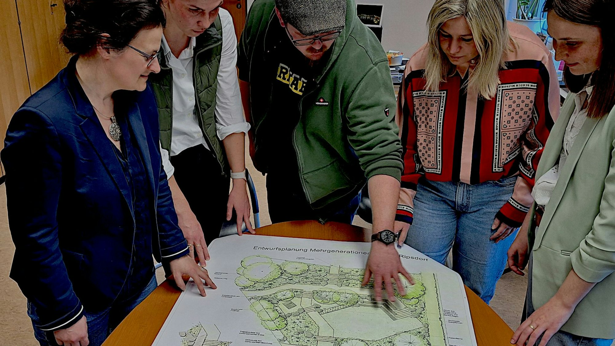 Fünf Personen schauen auf einen Plan, der auf einem Tisch liegt.