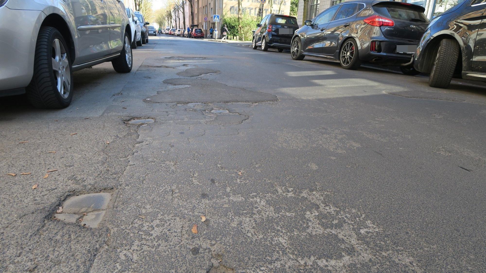 Aus der Froschperspektive aufgenommenes Bild, das die Löcher und Flicken im Asphalt einer Straße zeigt